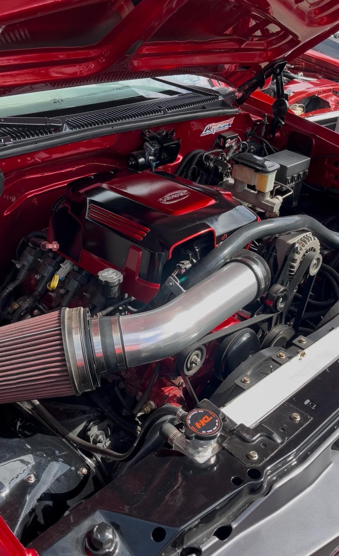 Compartimiento terminado del Chevrolet Tahoe con el LS2 6.0 instalado, tapa pintada en rojo y negro, tubo de admisión pulido y filtro cónico