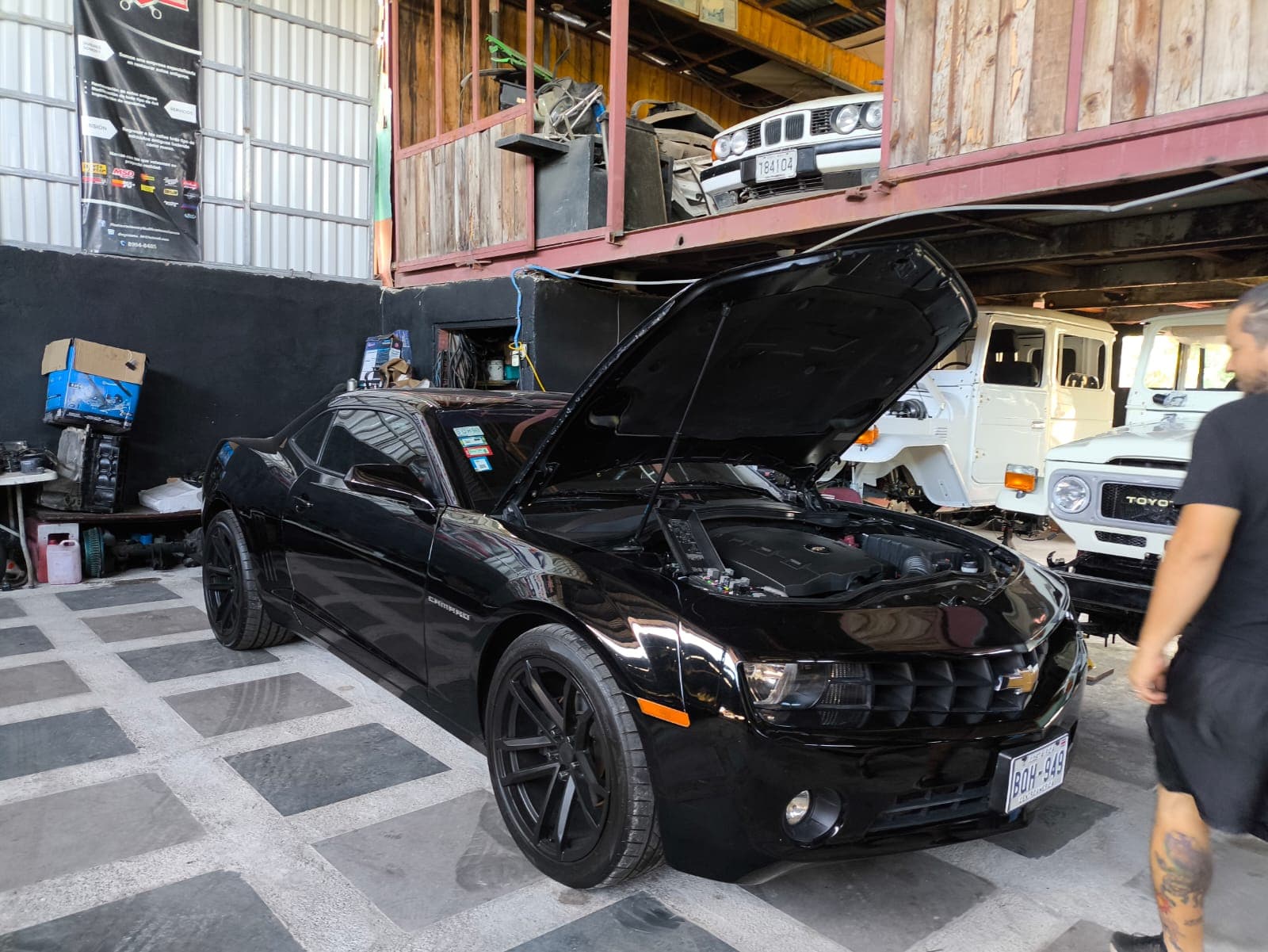 Chevrolet Camaro 2012 negro estacionado con el capó abierto en el taller de A1 Motors Tico Swap, antes de empezar el swap a LS3