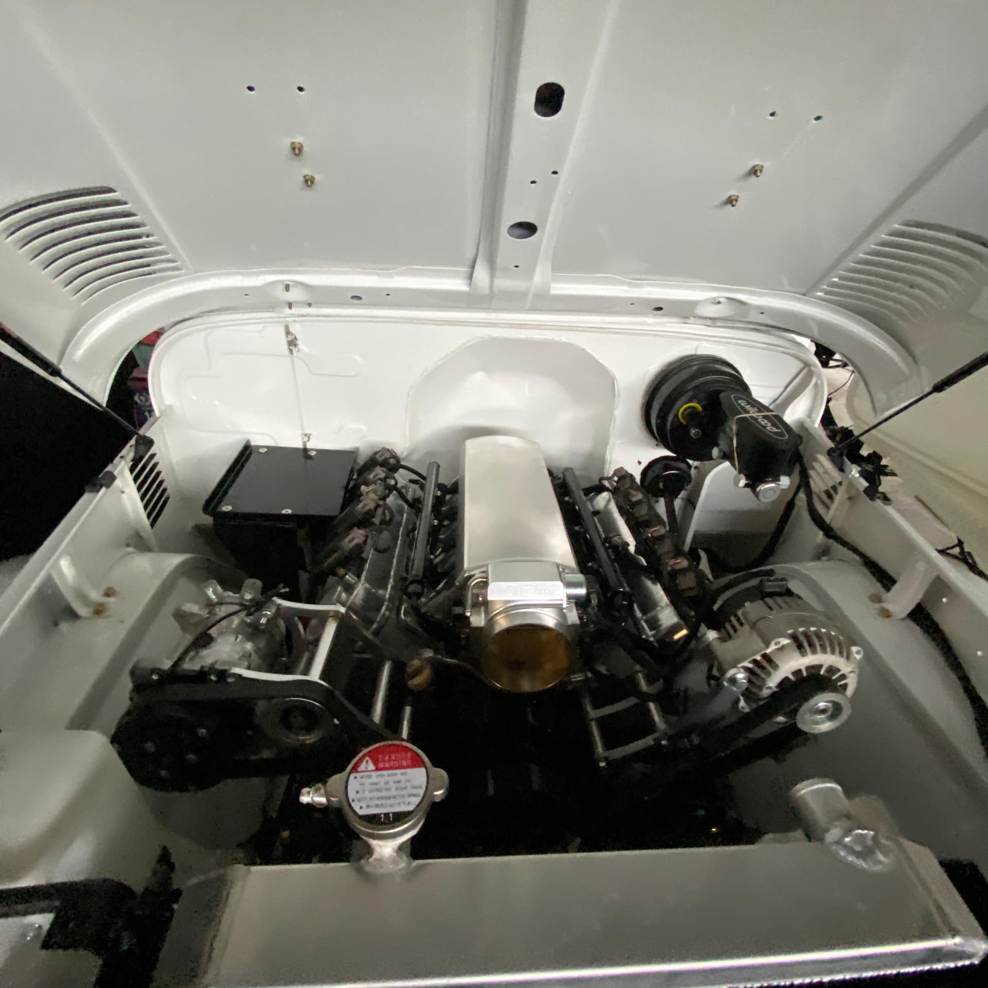 Compartimiento terminado del Toyota Land Cruiser BJ40 visto desde arriba, todo pintado de blanco, con el LS 5.3 centrado y la bomba de frenos Wilwood