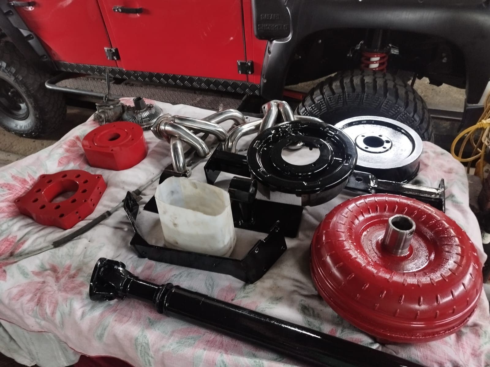 Piezas del tren motriz preparadas y pintadas junto al Defender: convertidor de torque, cardán, soportes, platos de freno y los múltiples de escape
