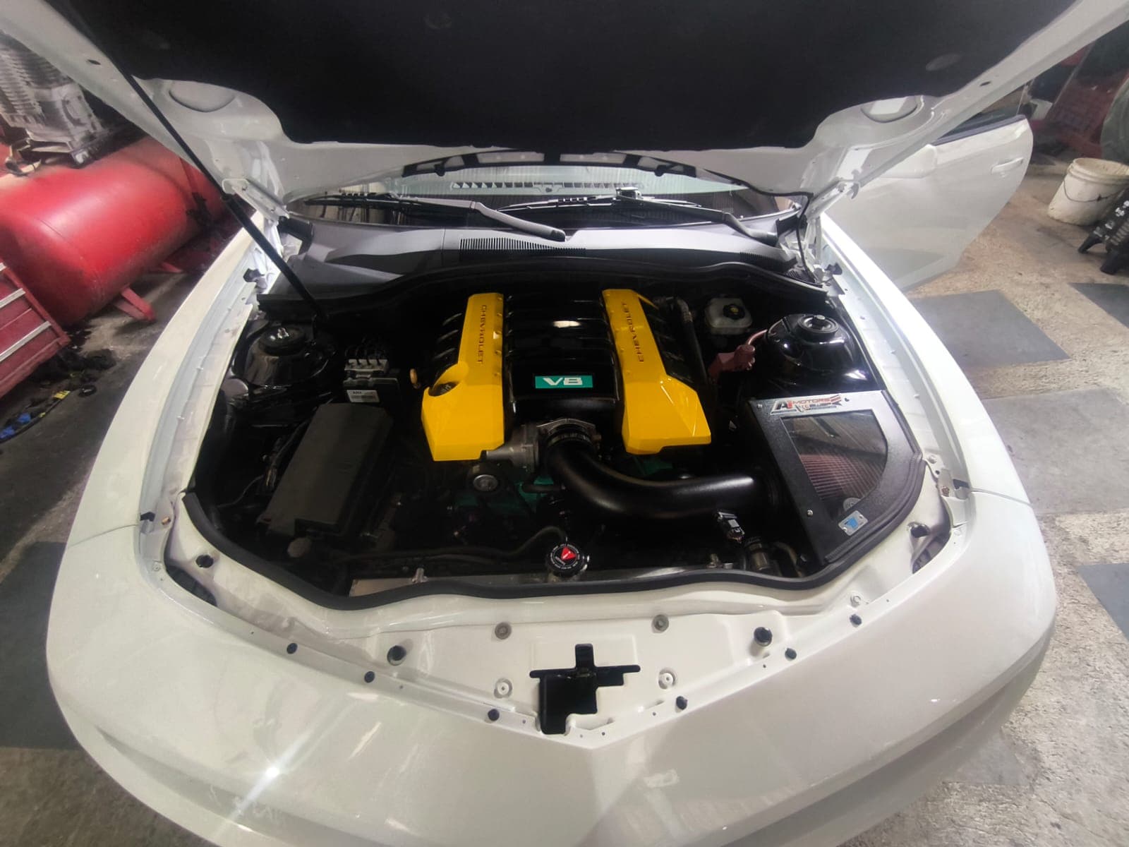 Compartimiento del Chevrolet Camaro ya repintado de blanco, con el V8 LS3 6.2 instalado, tapas Chevrolet amarillas y caja de aire de alto flujo