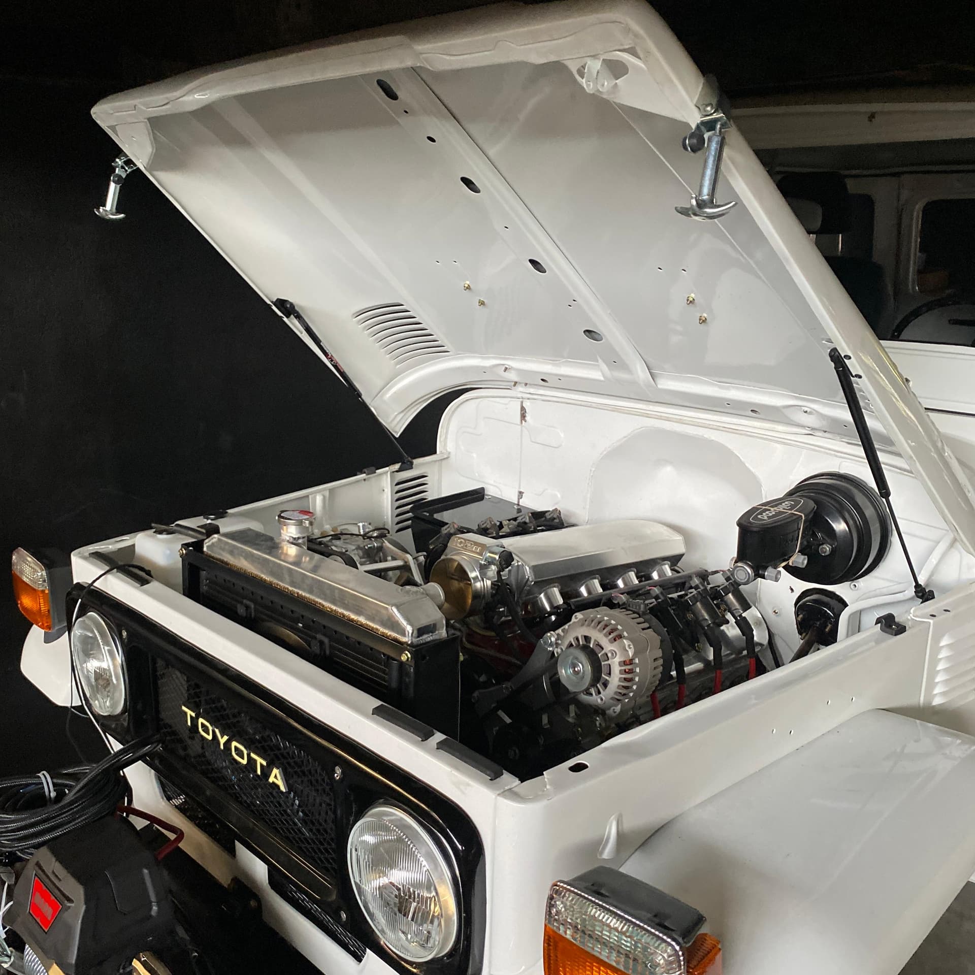Toyota Land Cruiser BJ40 blanco con el capó abierto en el taller de A1 Motors Tico Swap, con el V8 LS 5.3 instalado y la parrilla Toyota original