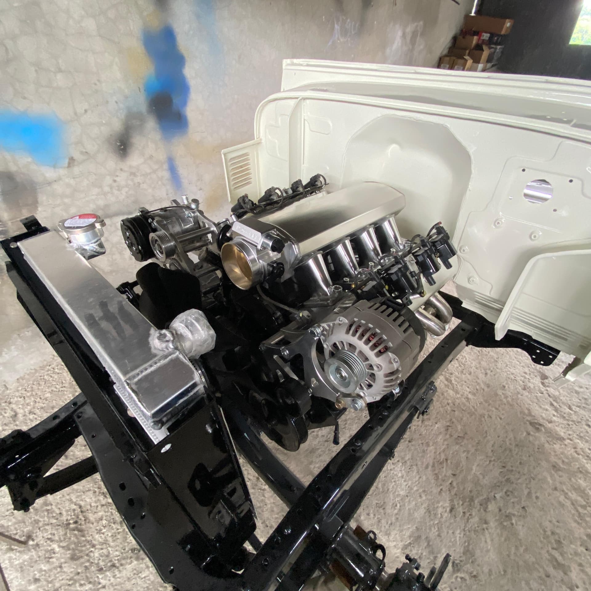 El LS 5.3 montado sobre el chasis pelado y pintado de negro del Land Cruiser BJ40, con el radiador de aluminio instalado y la carrocería blanca recién pintada al fondo