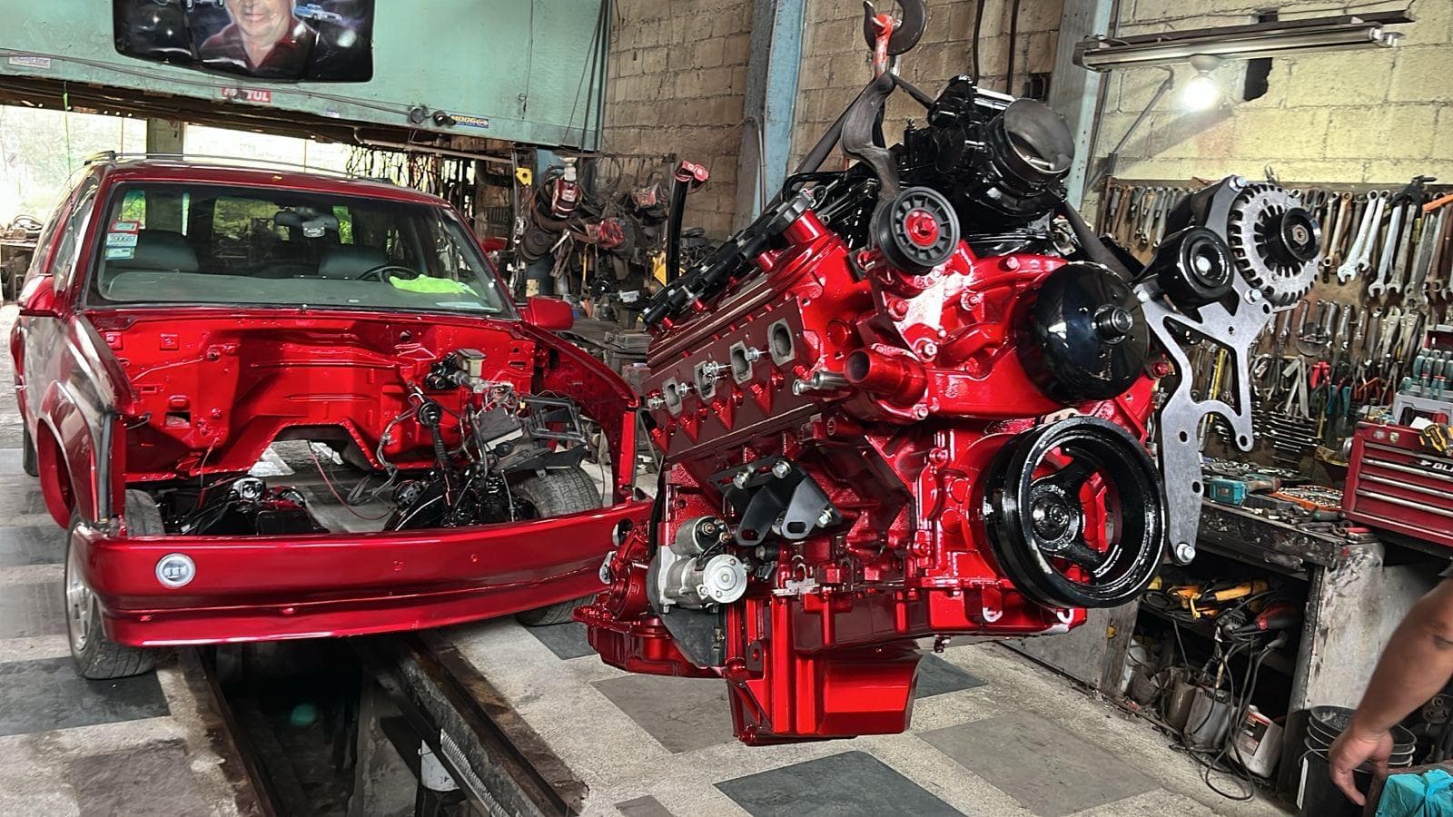 El Chevrolet Tahoe rojo con el frente desarmado y el conjunto de motor LS2 y caja 4L60 colgando de la grúa, todo pintado en rojo